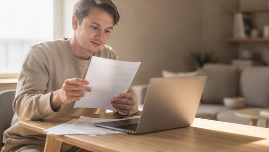 Person prüft am Schreibtisch ein Dokument neben dem Laptop – Grundbuchauszug kostenlos oder kostenpflichtig?